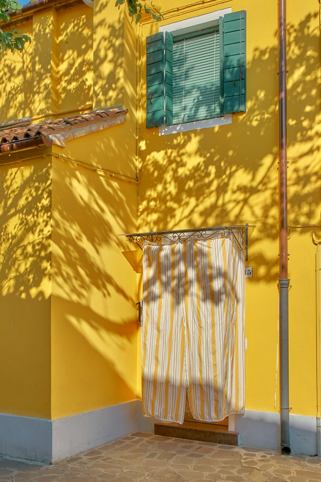 photograph of a yellow house with a window and curtain in the style of Murano, Italy, playful shadows, striped fabric, vibrant colorful architecture, detailed shadows –ar 85:128