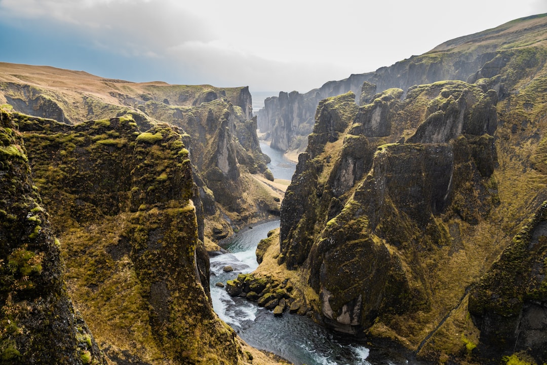 Photograph of FjardarLegacy in Iceland, a view from above looking down at the river running through an ancient canyon with mossy cliffs, a beautiful natural landscape, award winning photography, in the style of National Geographic. –ar 128:85