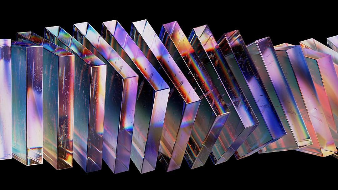 A row of differently shaped and colored rectangular prisms made of glass, all reflecting the same iridescent rainbow color pattern against a black background. The photography has a hyper realistic style.