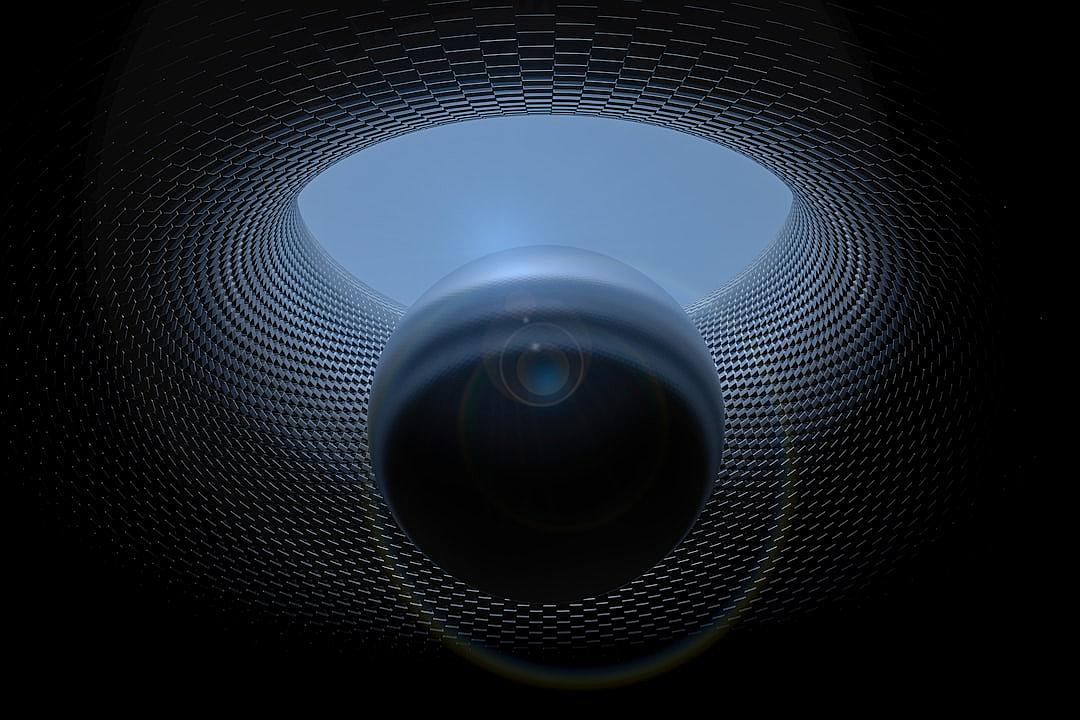 A wideangle view of the camera’s lens inside an empty black and blue tunnel, surrounded by circular mesh texture walls. The sky is visible through one opening in the ceiling. A single large round object with a glowing light sits at its center, creating a mysterious atmosphere.