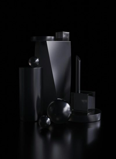 A dark, matte black background with various geometric shapes and objects placed on it. The shapes include spheres, cubes, cylinder boxes, squares, etc., all rendered in the same style. They have glossy textures that reflect light to give them an elegant appearance. There is also one large cube at the front of the composition. This is a product photography setting with the focus being centered around these metallic forms in the style of product photography.