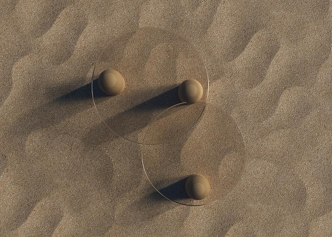 Three spheres floating on top of each other in the sand, aerial view, simple shapes, natural light, in the style of photorealism.