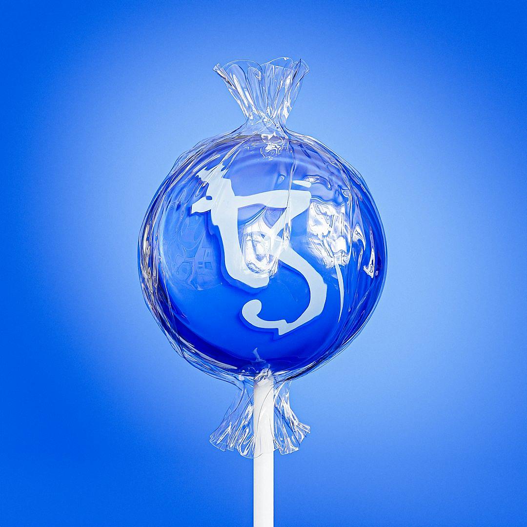 A blue lollipop with the white “T5” logo in transparent glass on top, against a solid blue background. The candy is wrapped and has no other decorations. It’s placed at an angle of about one third from above, looking like it was thrown up into air.