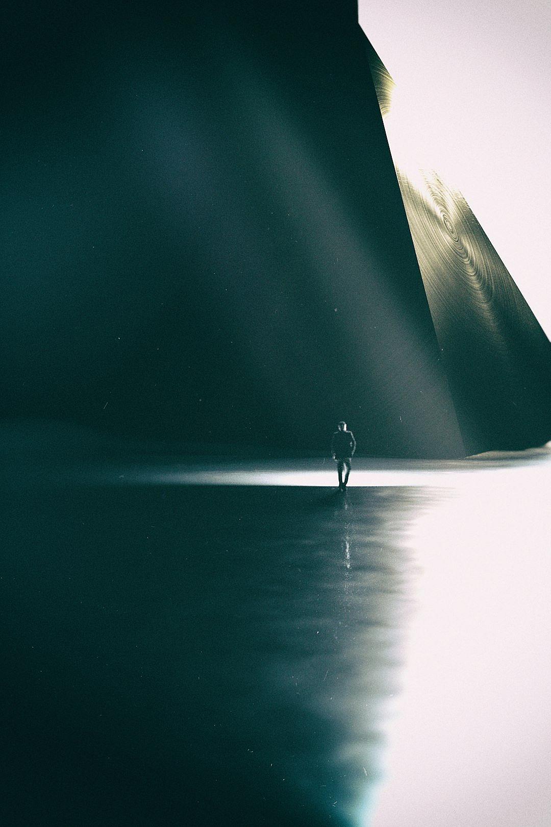 minimalist photography, man in the distance with his dog standing on water surface at night, reflection of huge dark triangular shape above him, volumetric light rays, dark grey and white tones, shadow play, minimalism,