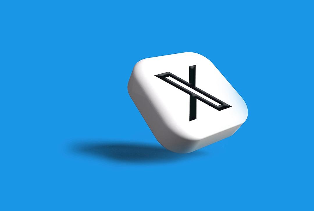 A white cube with the letter “X” on it, floating in midair against a blue background. The icon is designed in the style of an illustration and features a black line outline. It has a square shape and its surface looks matte. There is no shadow underneath or a soft gradient color palette. This design symbolizes minimalism and simplicity.