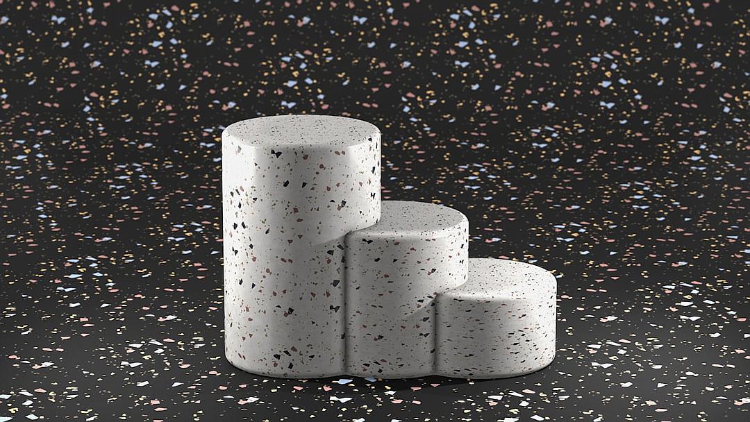 A set of three white terrazzo cylinder podiums on black background, with speckles in various colors, placed against each other to create an illusionistic effect. The backdrop is scattered with small particles that add depth and texture to the scene. This design showcases the beauty and diversity associated with terrrika se ornamental concrete.