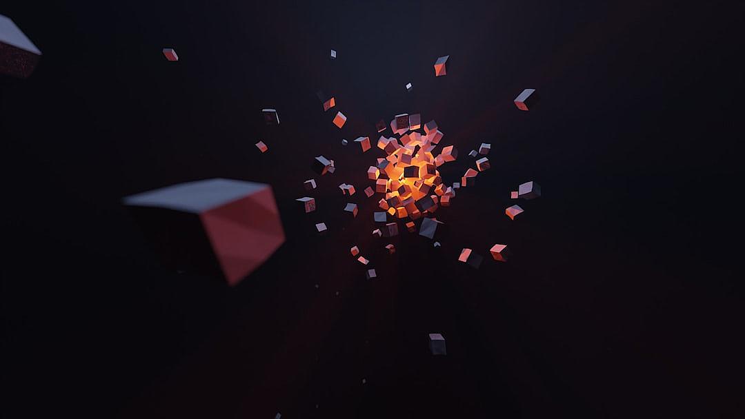 A dark room with low poly cube particles floating in the air, the center of which is an orange glowing sphere made up of small cubes. The cubes have red and white edges and some appear to be breaking apart from one another as they float around it. It’s a very simple yet powerful scene.