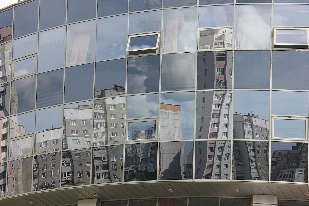 In the city of St exhangel, on Krestiko Street in front of the V inch bank building, the facade had large glass windows reflecting other buildings and the sky. The reflection showed lowrise apartment blocks and modern highrises. In one window you could see an old multistory house from the early 20th century, which was attached to another new skyscraper in the style of walls of concrete. It was summer outside and there were clouds visible through the glass. This photo was taken with a Canon EOS R5 camera using a macro lens.