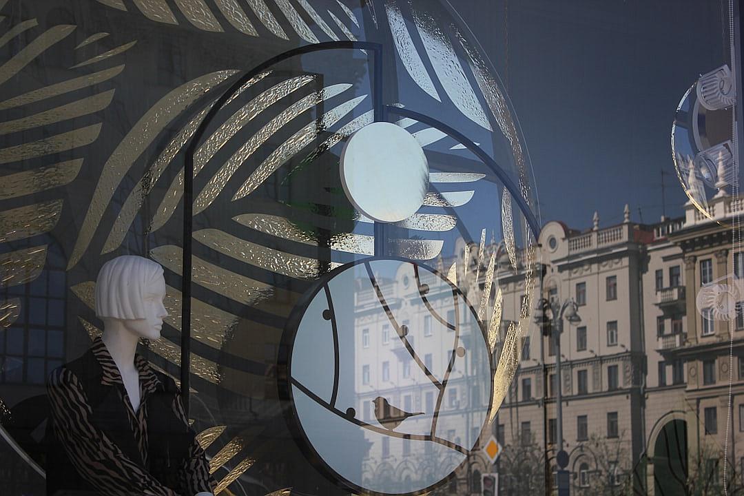 digital art of a window display in Milan, featuring an artistic installation with large circular mirrors and mannequins wearing black zebra pattern , surrounded by classical buildings. The design incorporates silver grey and dark navy blue tones, creating a harmonious blend between modern fashion and architectural elegance. In the background is a reflection of the cityscape of Piazza duomo.