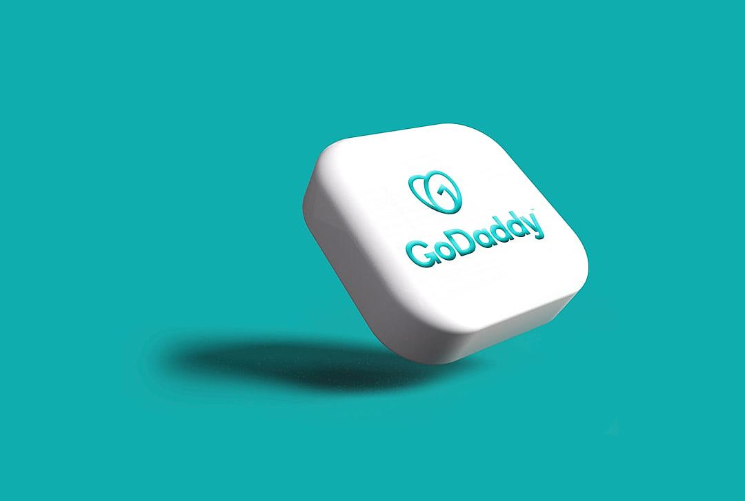 A white, square shaped text button with the word “GoDaddy” in teal floating mid air on an isolated background. The design is simple and minimalistic with subtle shadows under its edges that give depth to the shape with round corners and rounded edges. A small logo or icon representing cloud technology can be seen on one side of the button in the style of minimalism.