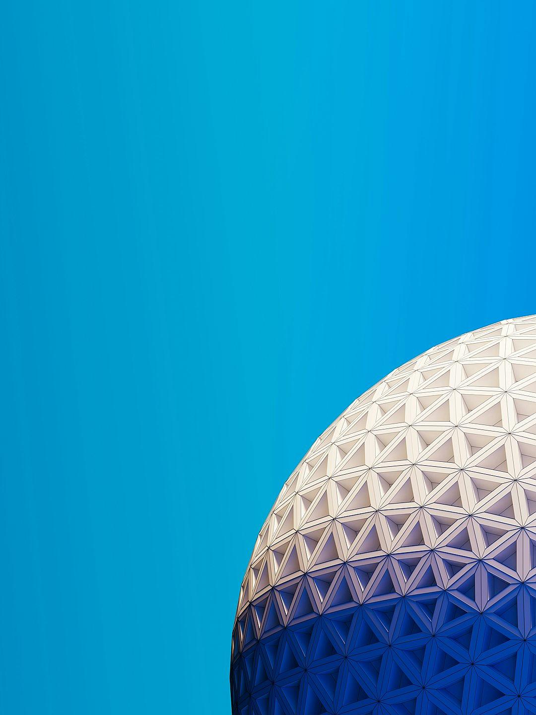 A close up of the Epcot ball at Disney World with a blue sky background. The design is simple and minimalistic with white space in the center for text. Geometric shapes and clean lines are used with high resolution and no shadows for high detail. It has a flat design with a bright color palette and blue color theme. The image uses high contrast with white on a dark blue background in the style of vector art. Natural lighting is used to create a hyper realistic style.