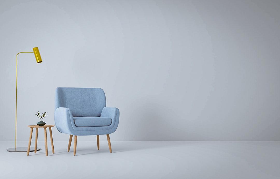 Minimalist plain white background for product photography with just one blue armchair and side table, a grey floor lamp, lots of light from the right hand side, a grey wall in the background.