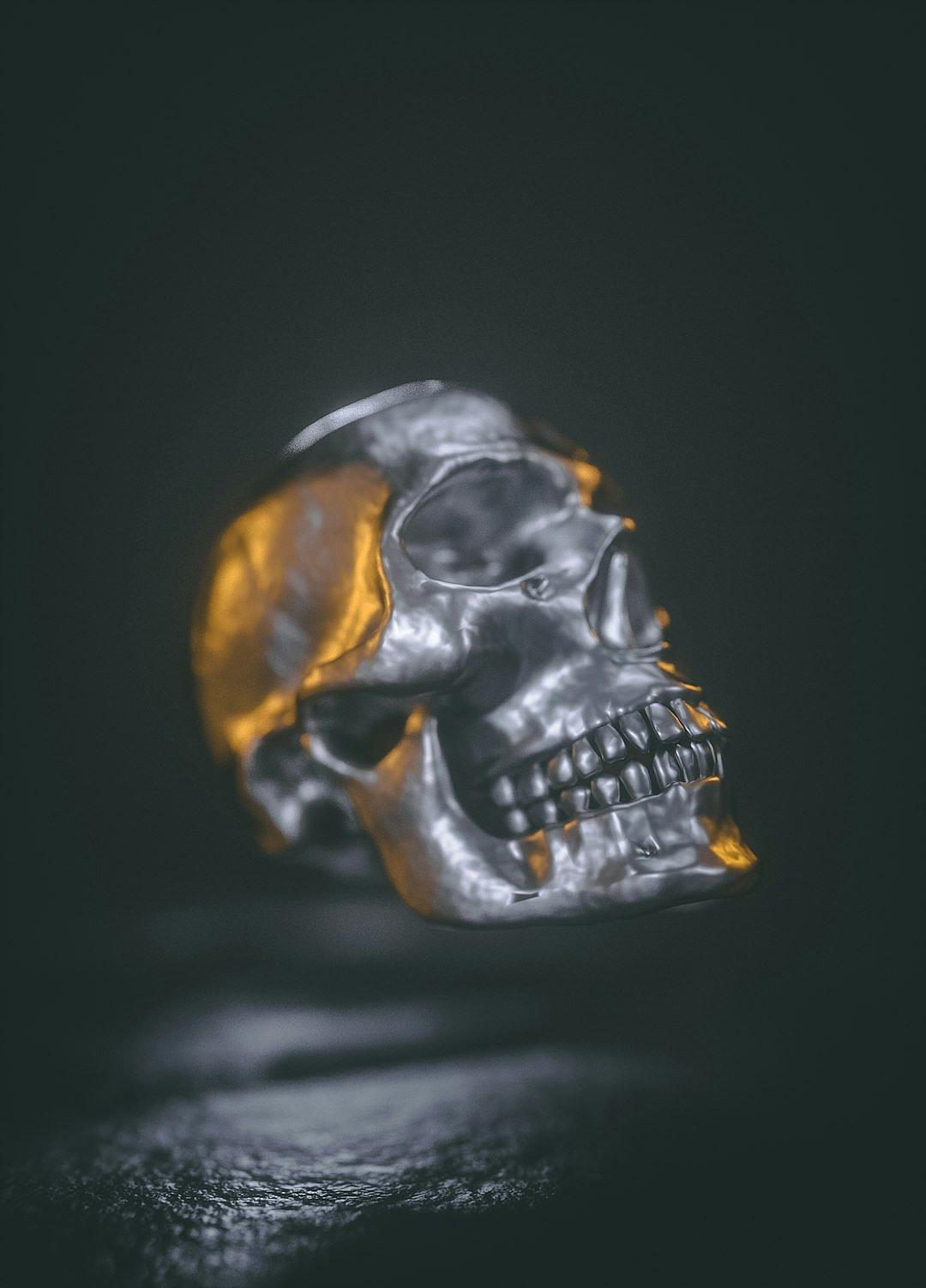 Close up shot of a skull ring, made out of silver and yellow metal against a dark background with low key studio lighting in a minimalist, hard light and contrast cinematic style at high resolution with hyper realistic and super detailed rendering in the style of product photography.