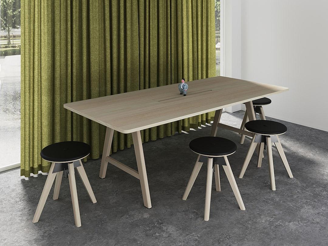 A modern, rectangular wooden conference table with four black bar stools around it. The light wood table has round black seat cushions on the bar stools. There are green curtains in front of them. It stands on a concrete floor in a Scandinavian style of interior design.