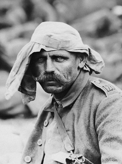 A photo of an old, tired German soldier in the trenches during World War I with his head covered by cloth and mustache