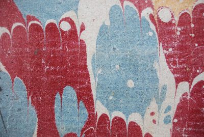 Close up of the texture of an antique red, blue and white marbled pattern on paper with paint drips in it. The texture shows the pattern in the style of traditional marbling techniques.