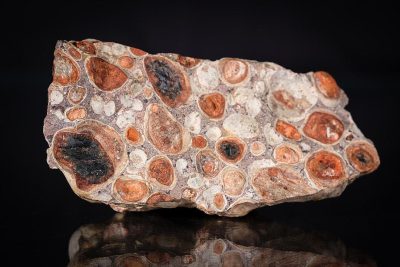 A large piece of chalcedony, with round and redish brown spots on it, is displayed against black background. The stone has intricate patterns and textures that give off an exotic feel. It's placed on the right side of the picture. There should be no other objects in front or behind the object. The focus is sharp and clear, highlighting every detail of texture and color of rock surface. This photo was taken using Canon EOS R5 camera with RF 2470mm f/8 lens at F3.6 aperture setting to capture intricate details.