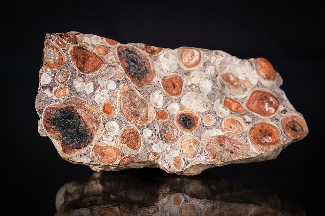 A large piece of chalcedony, with round and redish brown spots on it, is displayed against black background. The stone has intricate patterns and textures that give off an exotic feel. It’s placed on the right side of the picture. There should be no other objects in front or behind the object. The focus is sharp and clear, highlighting every detail of texture and color of rock surface. This photo was taken using Canon EOS R5 camera with RF 2470mm f/8 lens at F3.6 aperture setting to capture intricate details.