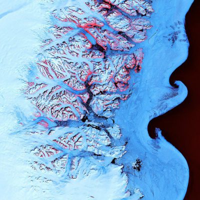 A satellite view of the Arctic with ice and snow, showcasing vibrant red river braids flowing through it. The topographic lines on both sides show mountains in blue tones, with a deep black ocean at their base. In pink color, there is an island that has emerged from the land due to global warming. This aerial perspective offers an immersive experience, providing a unique visual angle for National Geographic magazine covers in the style of their photography.