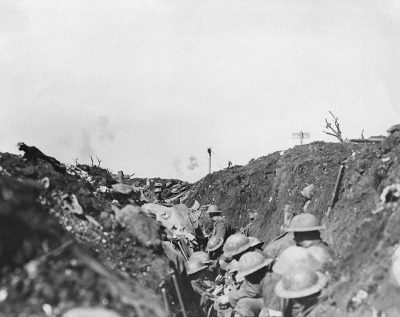 a black and white photograph of the trenches at TFITZ Allies in world war one, soldiers with gas masks on sitting down inside trench looking out into no man's land, large explosion visible far away