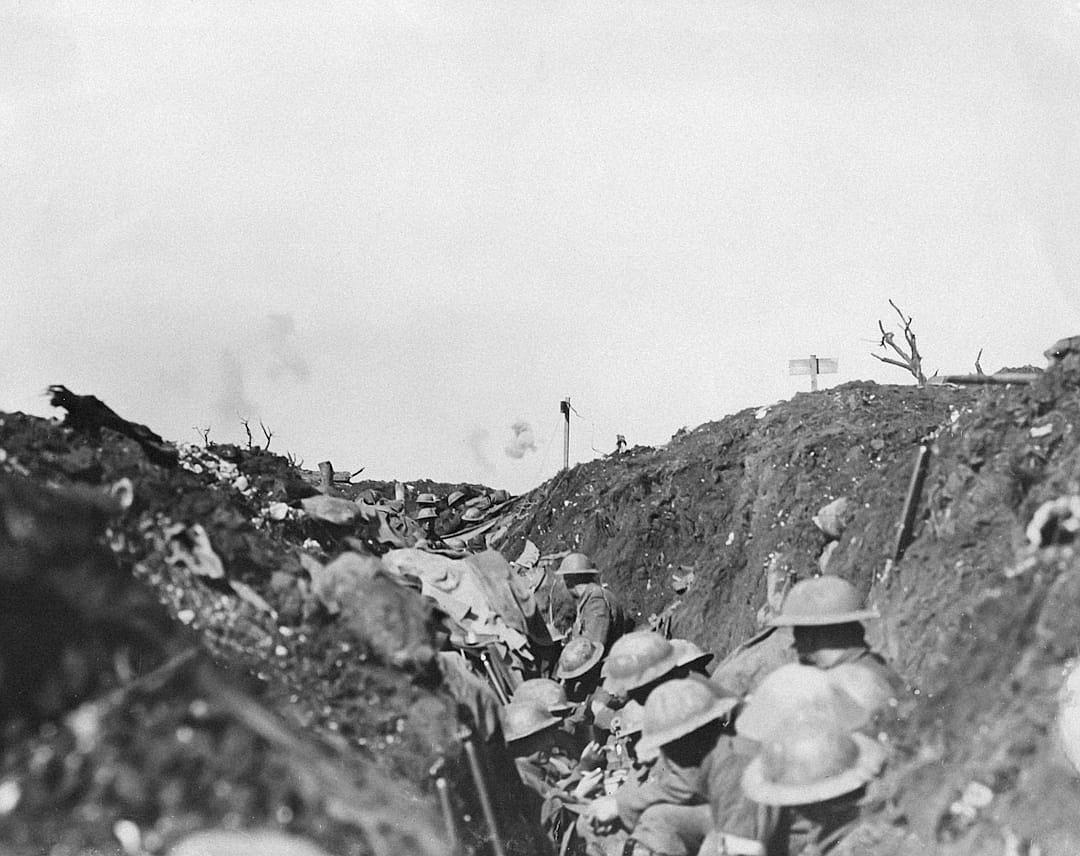 a black and white photograph of the trenches at TFITZ Allies in world war one, soldiers with gas masks on sitting down inside trench looking out into no man’s land, large explosion visible far away