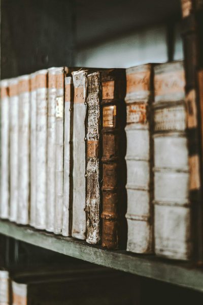 A closeup of antique books on an old wooden shelf, their spines weathered and textured with age, creating a nostalgic atmosphere in the library setting. The focus is sharp to capture every detail from hardcover covers to leatherwork, evoking curiosity about the stories within their pages in the style of antique books.