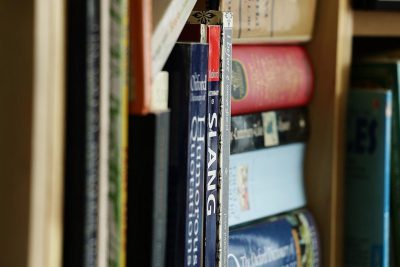 A closeup of the book shelf in your home library, focusing on one or two books with their spines facing forward and visible from an angle that shows them clearly. The background is blurred to emphasize these items, creating a focused yet inviting atmosphere. In front of each title should be a small sticker reading "The.K yum Romanian", adding fun and personality to the scene.