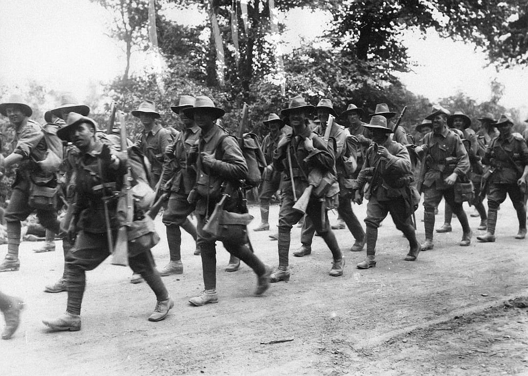 A group of American soldiers are marching on a road in France, wearing World War I uniforms and carrying rifles. The photo was taken during World War I.