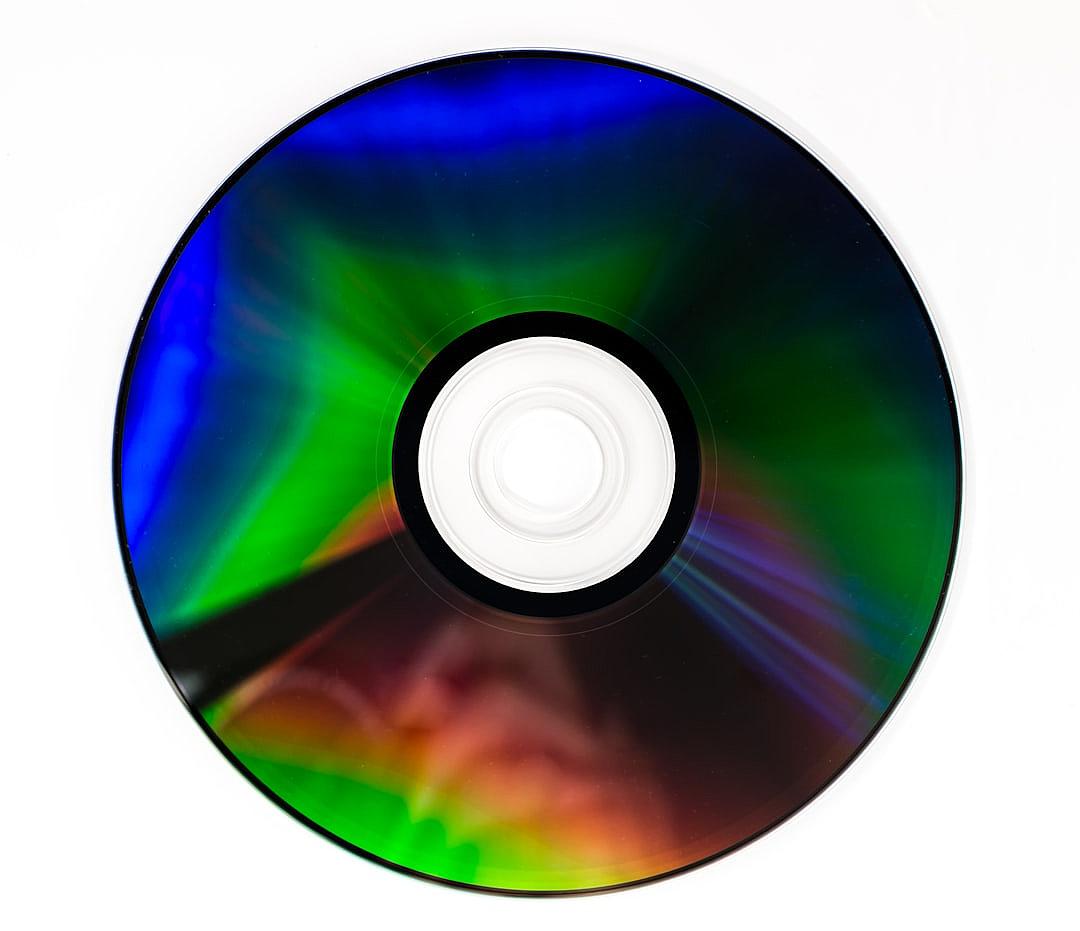 A colorful and vibrant high-resolution photo of a CD on a white background. The main focus is the bright green, blue, purple, red, and yellow hues. There is no visible text or letters in any part of the photograph. It is a full view of one small black disk with a white center, centered in the frame. This shot captures the essence of digital media technology, with sharp details and clear edges in the style of digital photography.