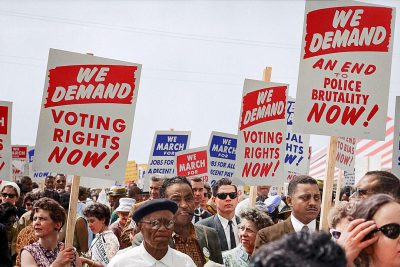 a photo of the march on Washington in which people holding signs say "WE DA neurons VOTE" and other sign says " we stomp police brutality now!" , colorized