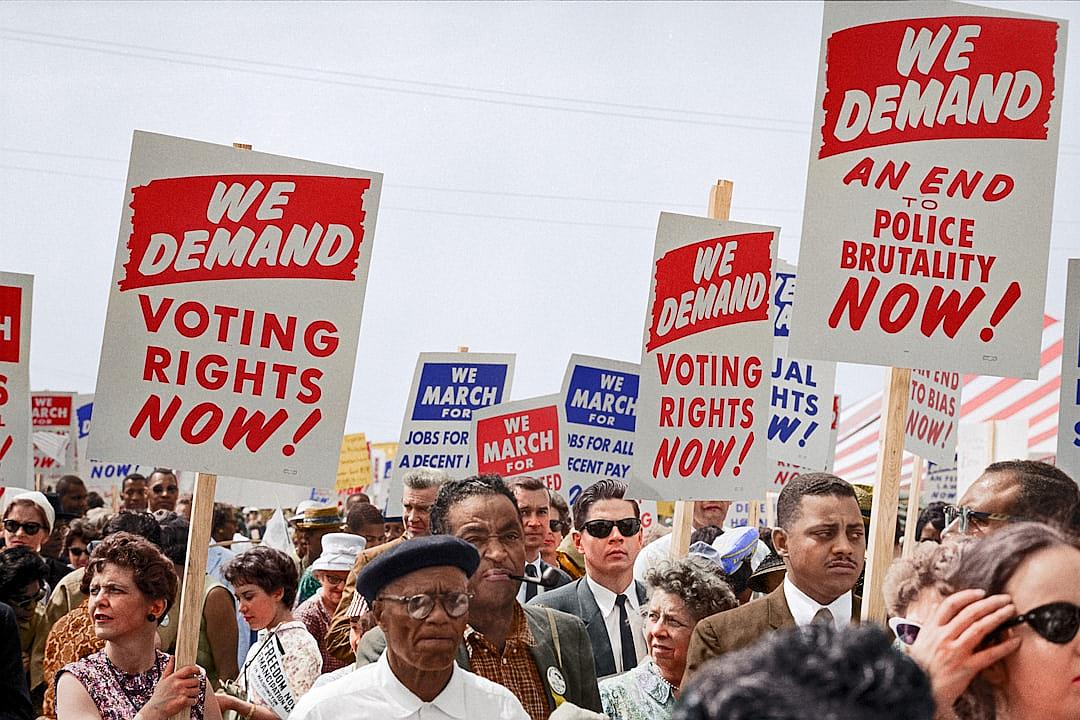 a photo of the march on Washington in which people holding signs say “WE DA neurons VOTE” and other sign says ” we stomp police brutality now!” , colorized