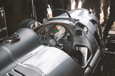 close up of silver le mans racecar with vintage dashboard, at the goodwood festival of speed in a crowd of people