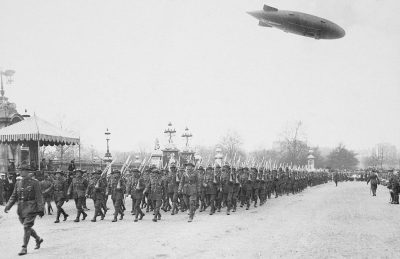 Black and white photograph of the WWI French heavy armored guard, marching in line through Champs Elysées Paris with an airship floating overhead. High resolution photograph with photo quality, in the style of an early 20th century photographer.