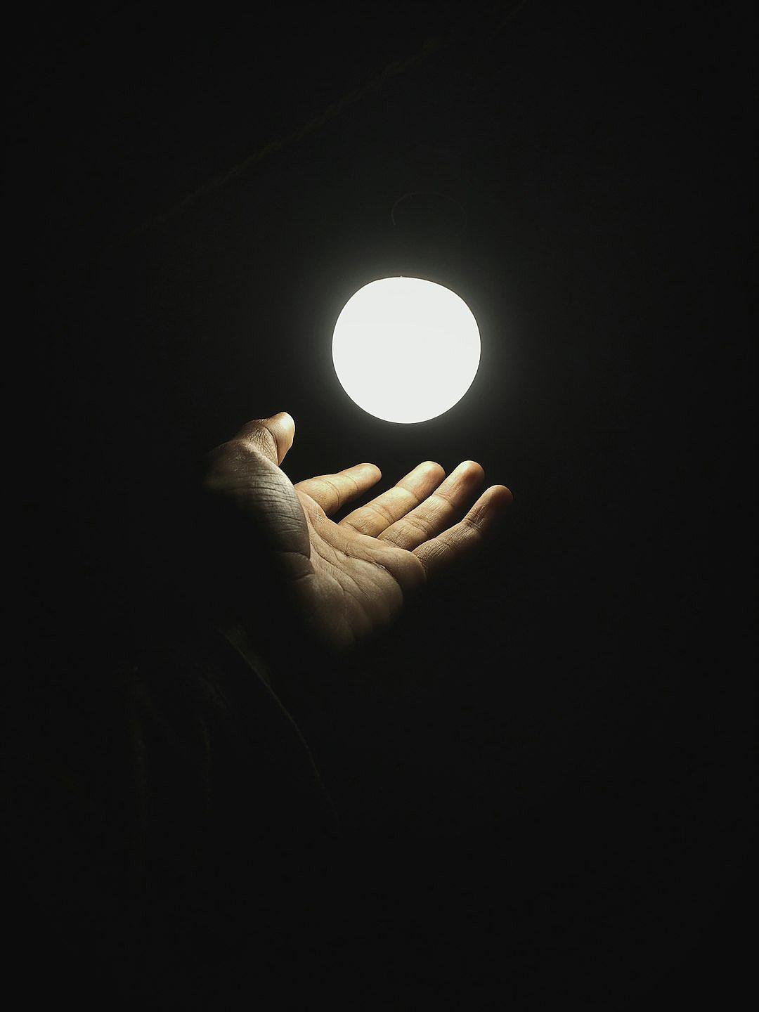 A hand holding up an illuminated ball in the dark, in a minimalist style in white and black.