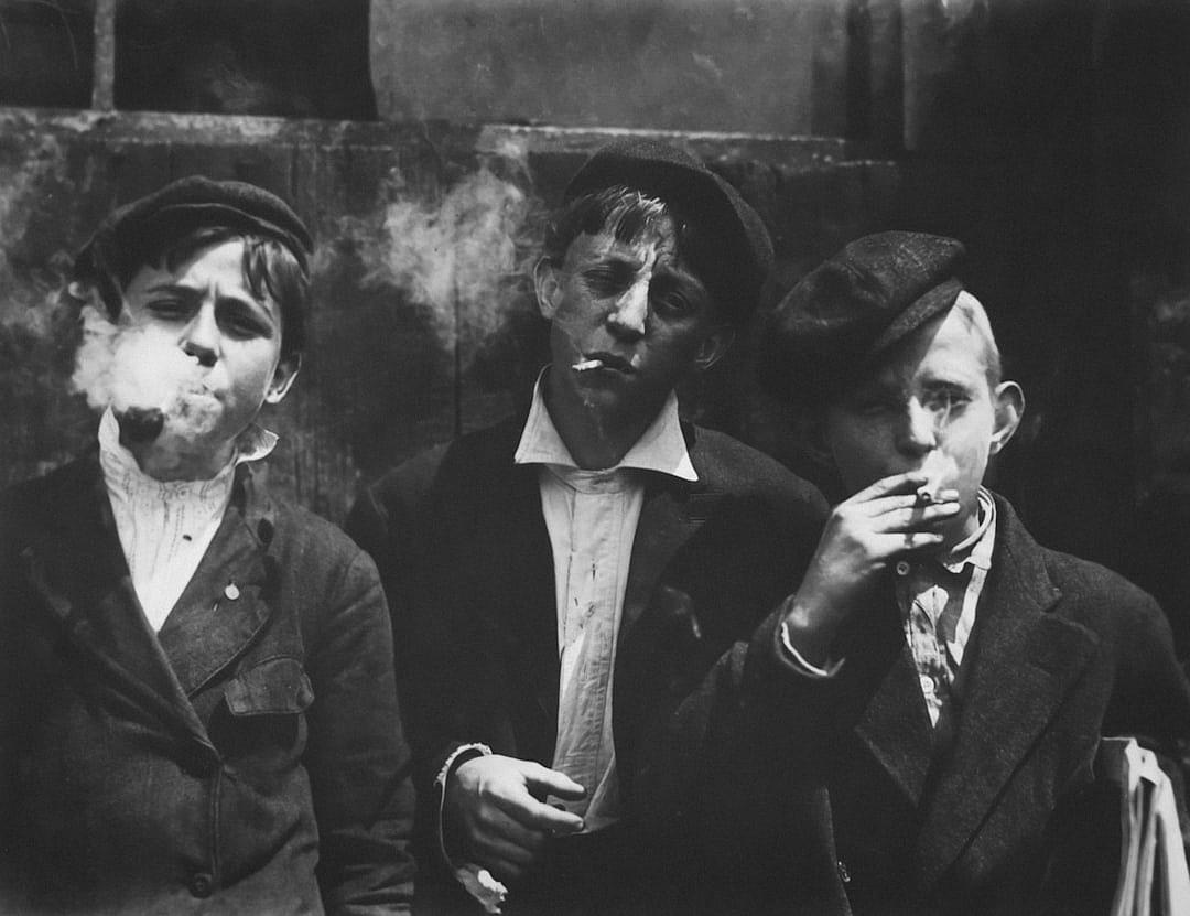 vintage photograph of three young working class boys smoking cigarettes in the streets, black and white photography in the style of roger f‐jullien, grainy film noir style