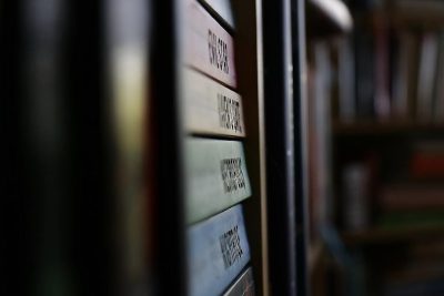 A closeup of the labels on books in an ancient library, highlighting their unique typography and design. The focus is placed on one book with its label prominently displayed against blurred shelves filled with other boxes and tomes. Soft lighting creates gentle shadows that accentuate details like decorative borders or handwritten signs. This shot highlights both the visual appeal and historical significance associated with such dusty but precious items as they line up along walls in endless rows. The style of this image is reminiscent of works in the style of early photographers who sought to capture details of ancient texts and libraries.