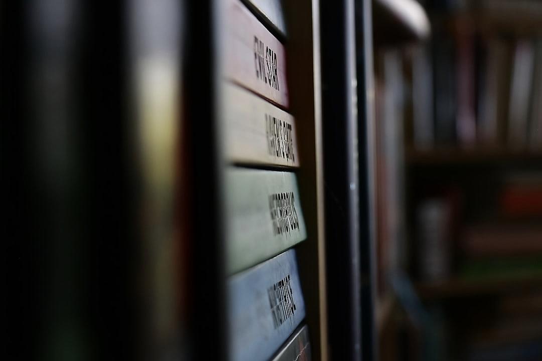 A closeup of the labels on books in an ancient library, highlighting their unique typography and design. The focus is placed on one book with its label prominently displayed against blurred shelves filled with other boxes and tomes. Soft lighting creates gentle shadows that accentuate details like decorative borders or handwritten signs. This shot highlights both the visual appeal and historical significance associated with such dusty but precious items as they line up along walls in endless rows. The style of this image is reminiscent of works in the style of early photographers who sought to capture details of ancient texts and libraries.