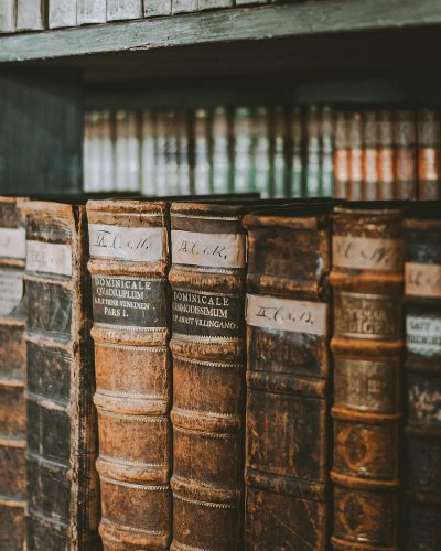 A closeup of vintage leatherbound books with handwritten labels, arranged on an old wooden shelf in the library. The soft focus and warm tones create a nostalgic atmosphere. Shot in the style of Canon EOS R5 at F8.046mm f/2.