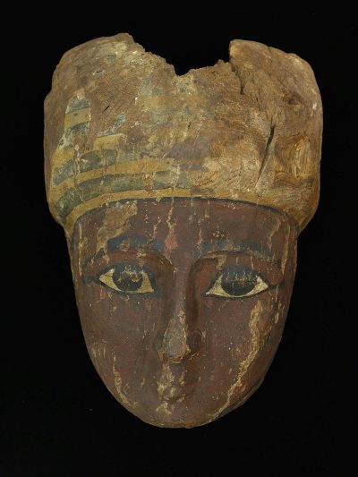 An ancient Egyptian woman's head, painted on wood and worn by time with no hair or eyebrows, carved out of an oval shaped piece of stone in the style of Hategic. A oakwood mask with gold edging around the eyes, painted face, small horns, black background.