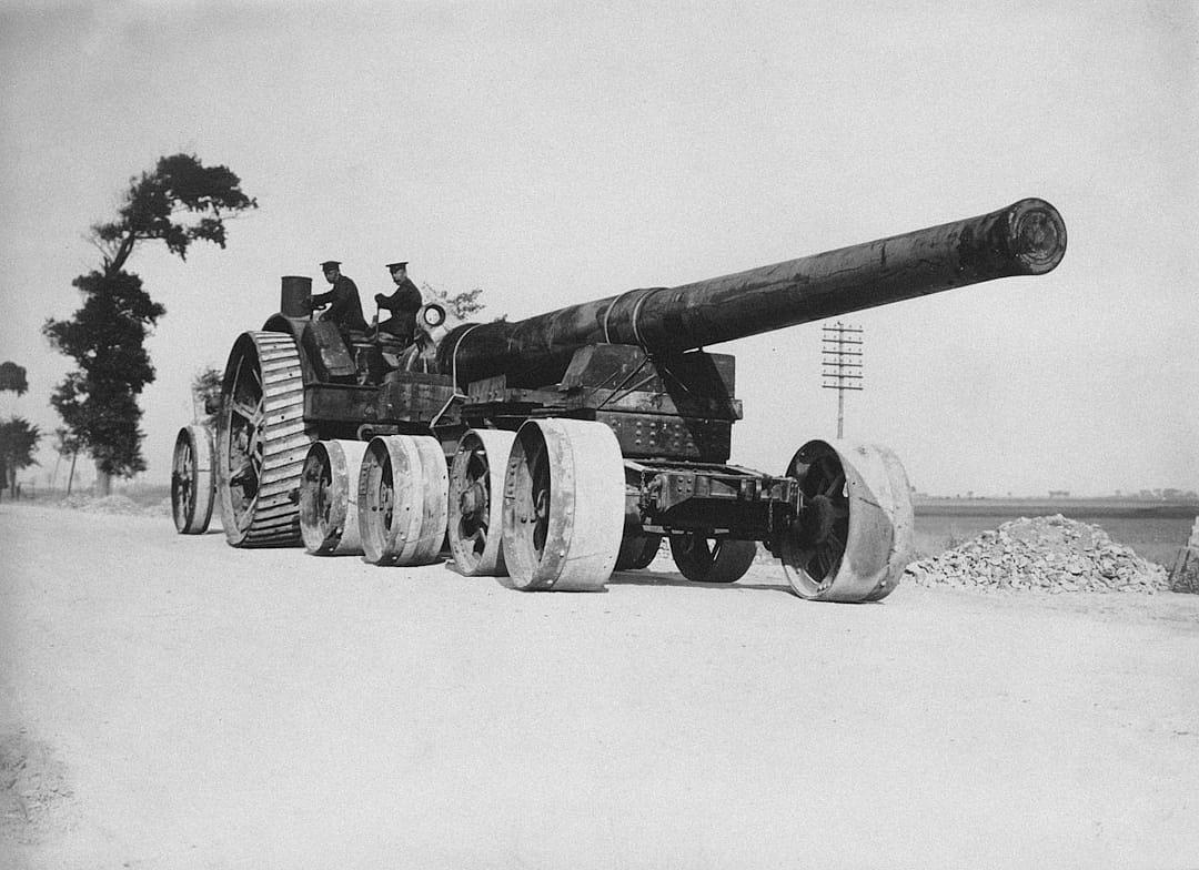 Old black and white photo of an oversized large long wide thick canon with wheels, standing on the side of the road in a quiet peaceful place, soldiers sitting at the top, horizon, in the style of an old photo.