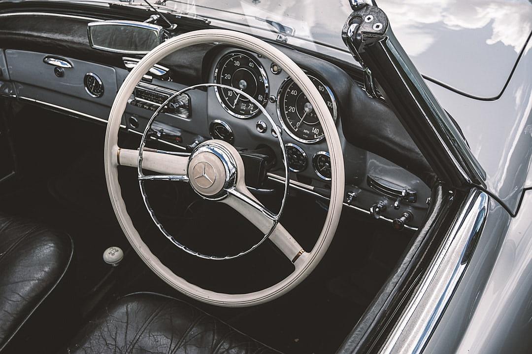 interior of vintage mercedes, silver wheel with white trim and black leather seats, vintage car show photography,