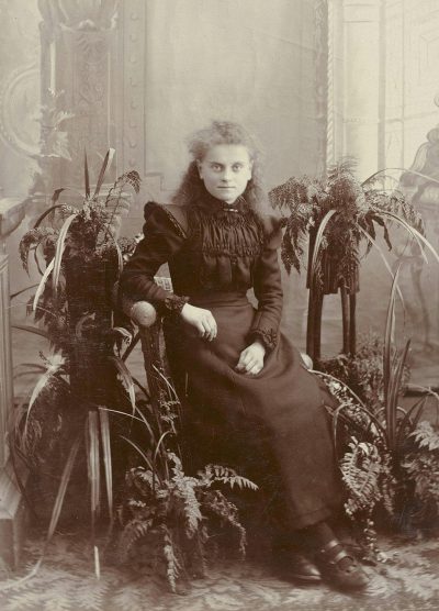 old photo, victorian woman sitting on chair with plants and ferns growing from it's sides, full body portrait, dark dress,