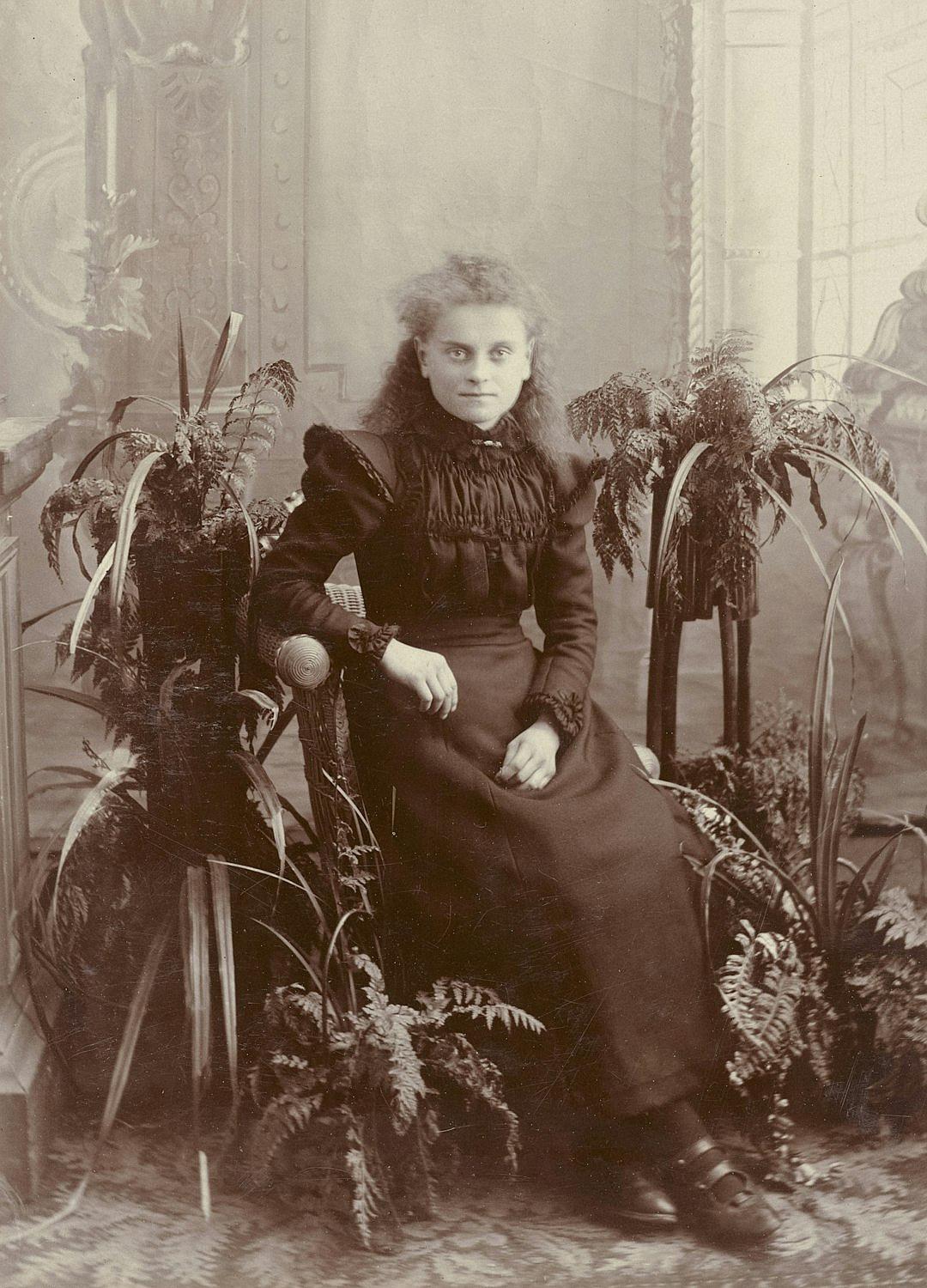 old photo, victorian woman sitting on chair with plants and ferns growing from it’s sides, full body portrait, dark dress,