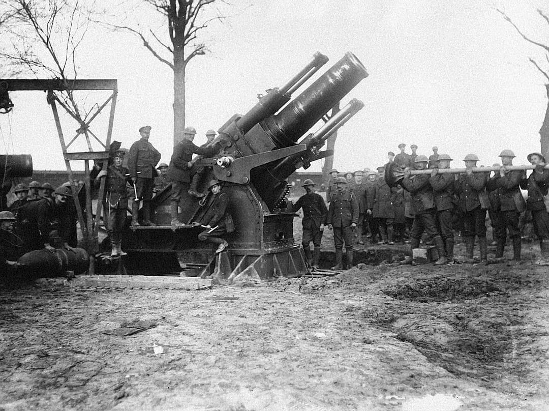 The heavy cannons of the first world war, being operated around them and set up in the field with soldiers standing next to them.