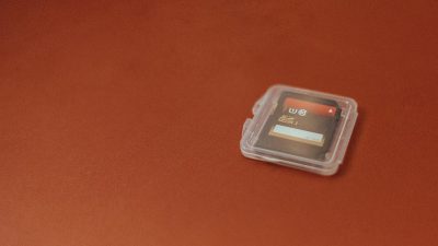 A small, clear plastic case containing an empty micro thread storage card is placed on the red table top. The background of the photo has no text or graphics and it is a closeup shot.