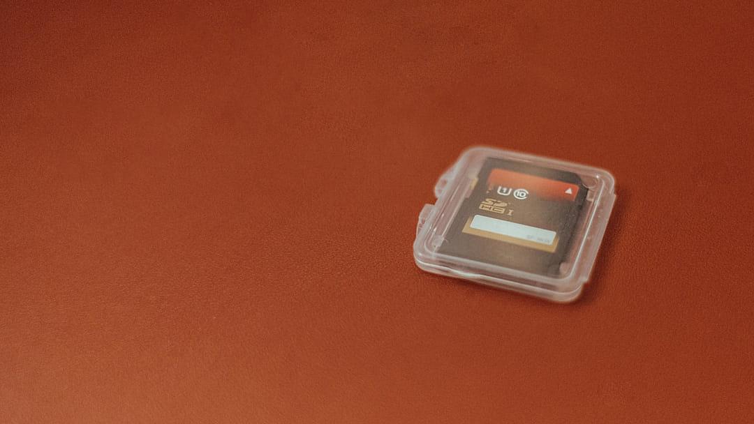 A small, clear plastic case containing an empty micro thread storage card is placed on the red table top. The background of the photo has no text or graphics and it is a closeup shot.