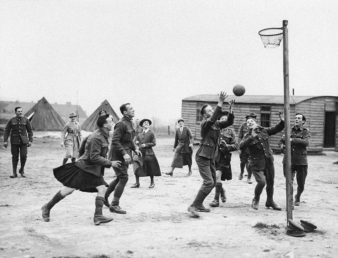 old black and white photo of British soldiers playing netball in a World War I military camp, women playing basketball with men in the style of various artists