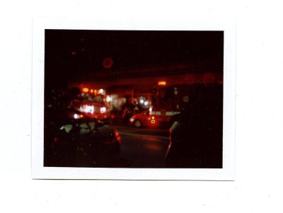 polaroid photo of fire truck and ambulances on the street at night, red lights flashing, taken from inside car window