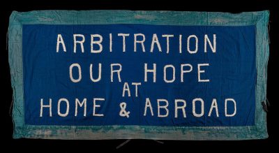 A blue banner with the words "Arbitration is our hope at home & Global" embroidered in white letters on it, 20th century cotton fabric flag.