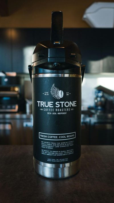 A black coffee pot with the words "Tesla true stone" on it, featuring an Americanstyle label design and logo for an advertisement photo shoot of a large stainless steel water keg filled with fresh beans from oneley's mountain rorocketry company called The Coffee RoMarkers Company based in Leesburg Vault National Park shot at Nikon Z6 II mirrorless camera using a NIKKOR Tl f/2 lens